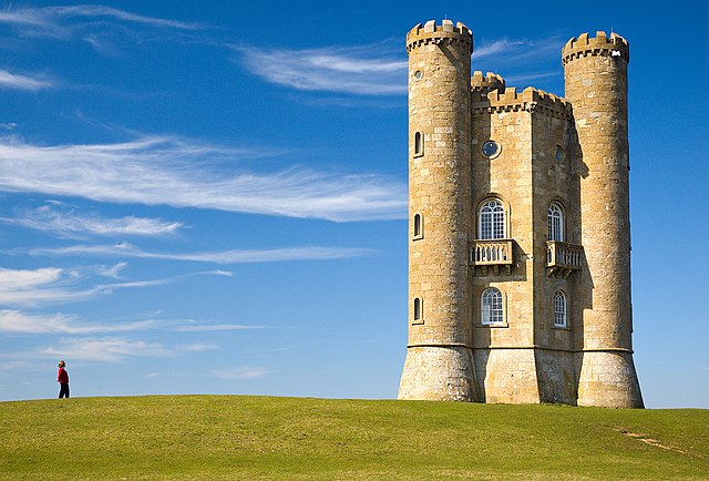 Green grass, on top of it a person in the left, a tower in the right and vast sky with a few clouds in
the background and middle.