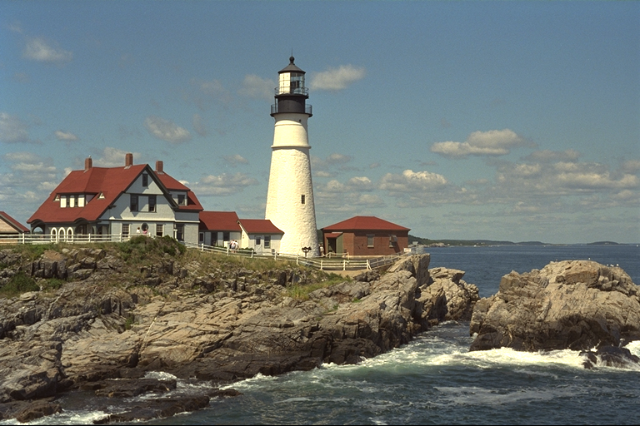 Houses with a lighthouse on top of a cliff above sea.